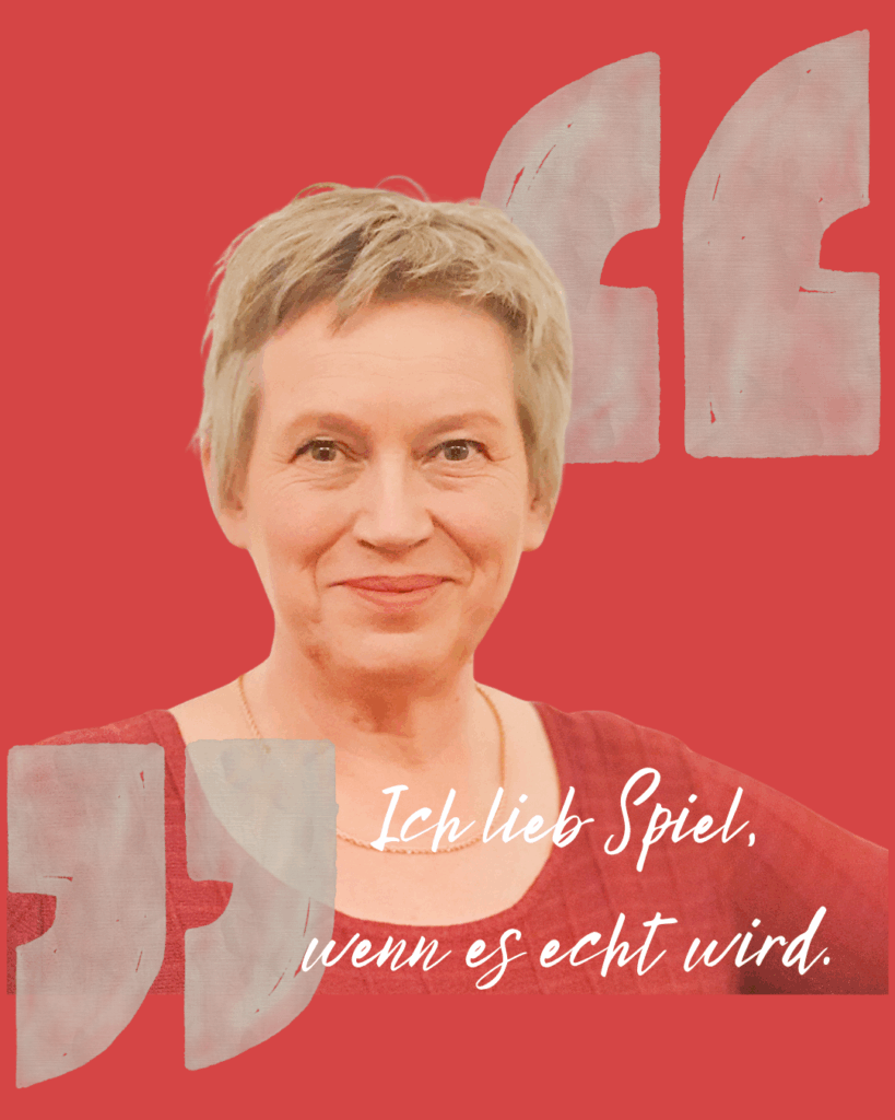 Silke Saracoglu lächelt selbstbewusst in die Kamera, vor rotem Hintergrund mit dem Satz „Ich lieb Spiel, wenn es echt wird.“ – Symbol für ihre Haltung: ehrlich, lebendig und kreativ.